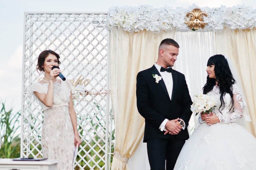 master of ceremonies making speech at wedding with bride and groom next to her. 