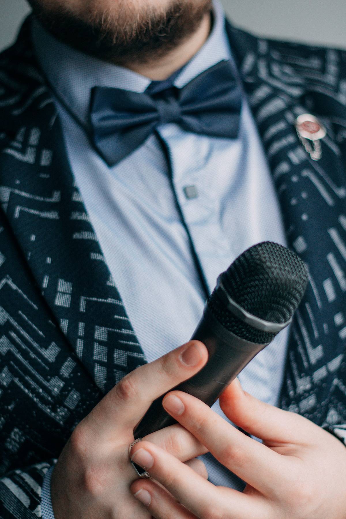 Master of ceremonies with microphone. Man with a beard and tie butterfly close-up. Business suit, speech and speaking, talk show, seminar spokesman.