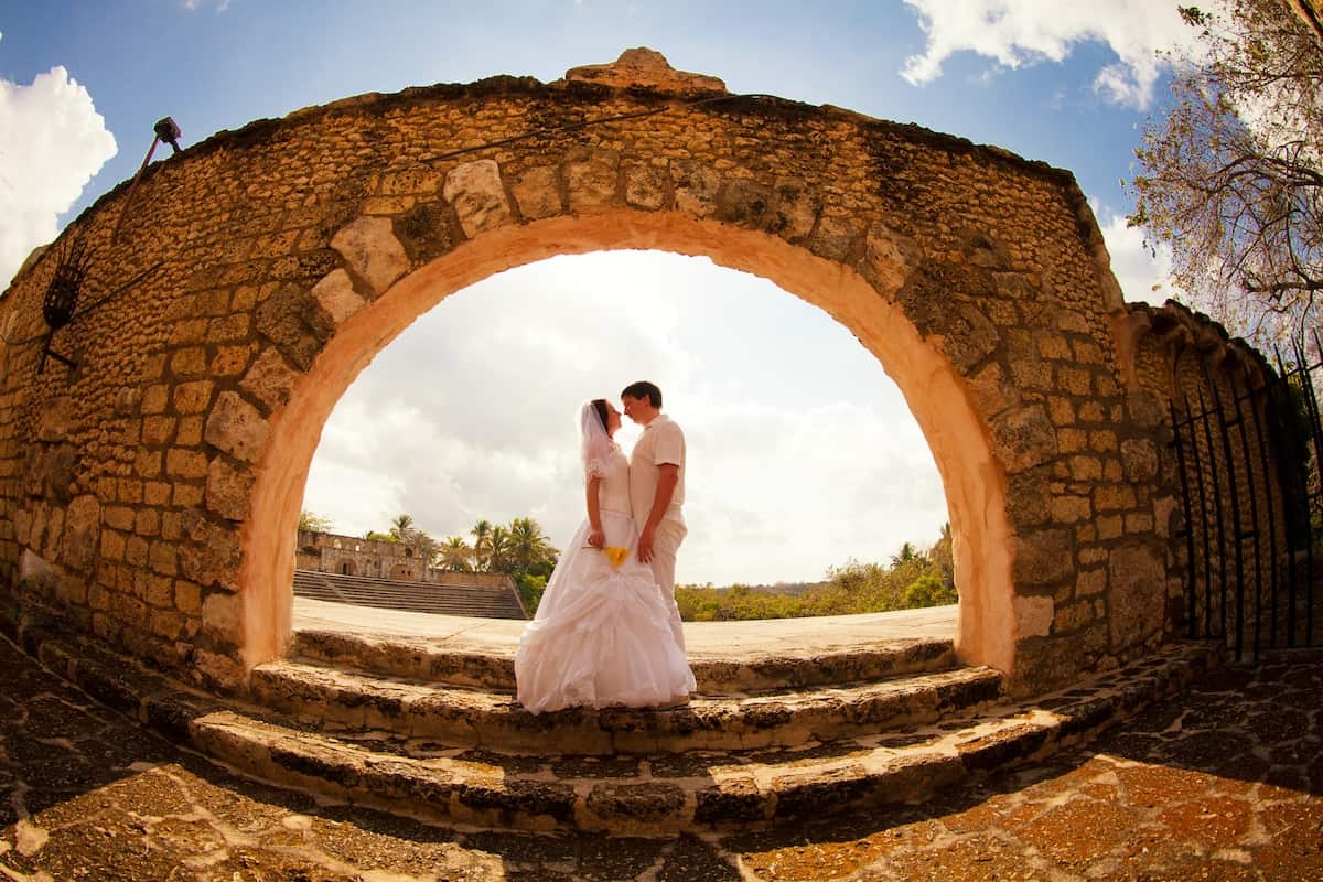 the couple in white wedding clothes stand at an old stone arch. honeymoon trip.